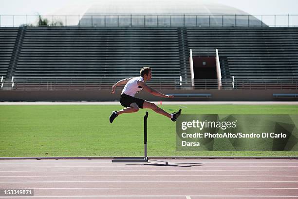 male athlete clearing hurdle, side view - hurdle race fotografías e imágenes de stock