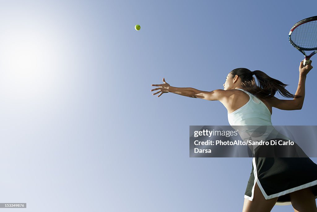 Female tennis player serving ball, low angle view