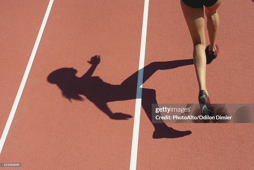 Female athlete running on track, low section, focus on shadow