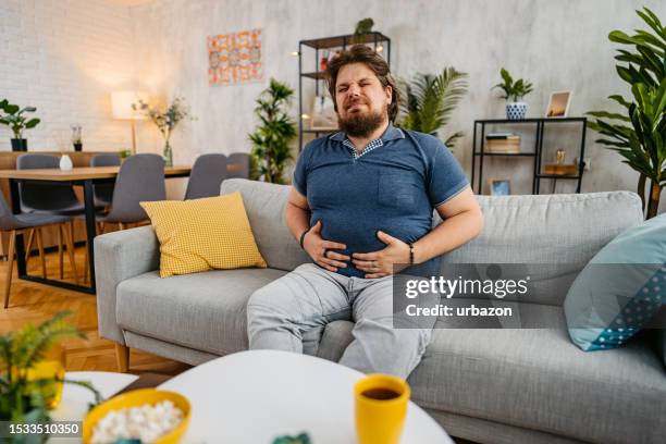 young man having stomach pain at home - fat guy belly stock pictures, royalty-free photos & images