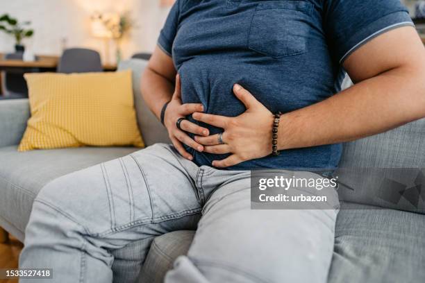 young man having stomach pain at home - appendicitis stock pictures, royalty-free photos & images