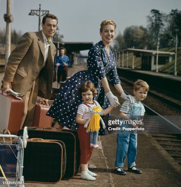 Family group of a husband, wife and two children stand with their suitcases and folded up pram on the platform of a railway station as they prepare...