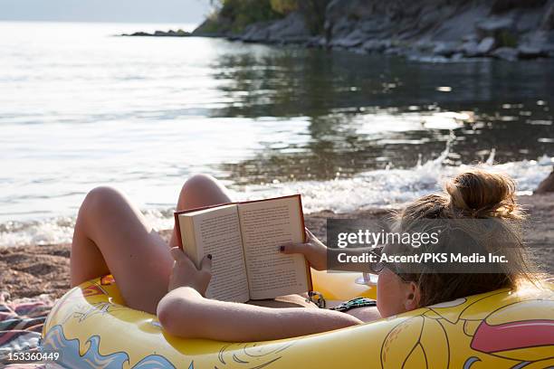 teen girl reads by lakeshore, in rubber raft - beach book reading stock pictures, royalty-free photos & images