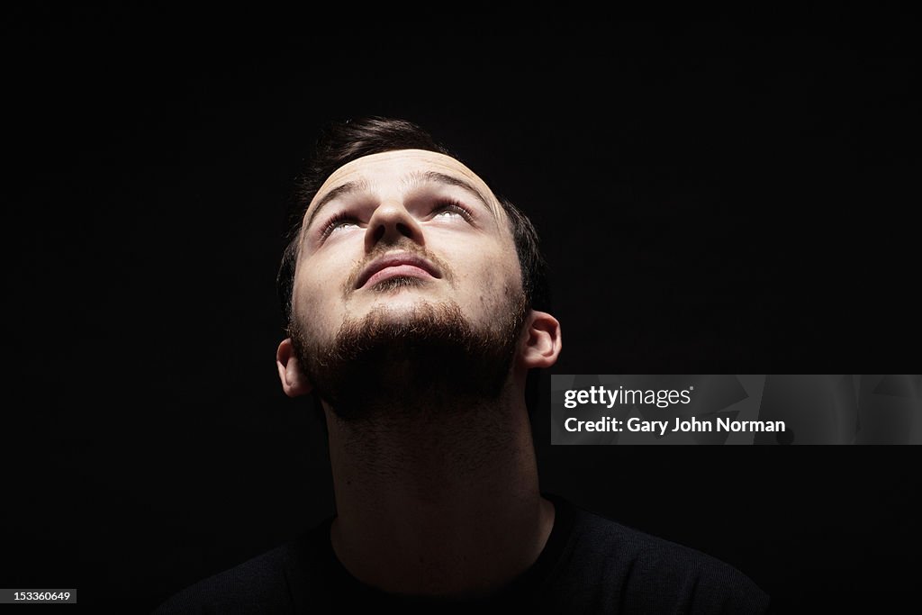 Young man against black background looking up