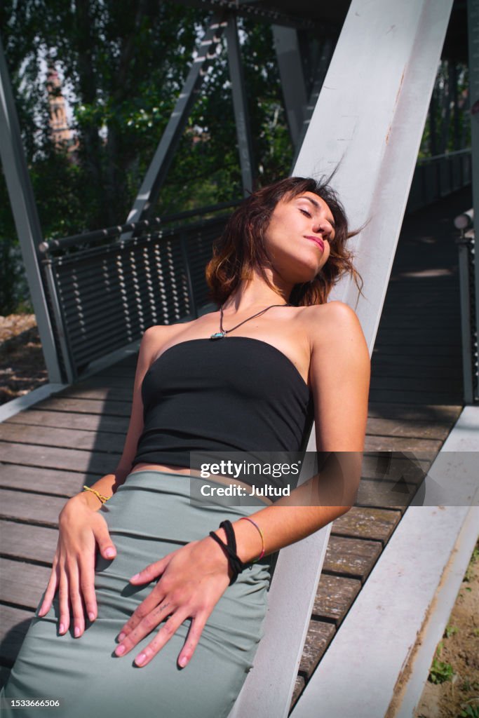 Portrait Of Young Woman Lying On Metal Girder Of Urban Footbridge