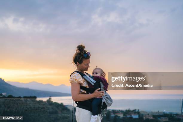 mother holds infant beside swimming pool - baby carrier stock pictures, royalty-free photos & images