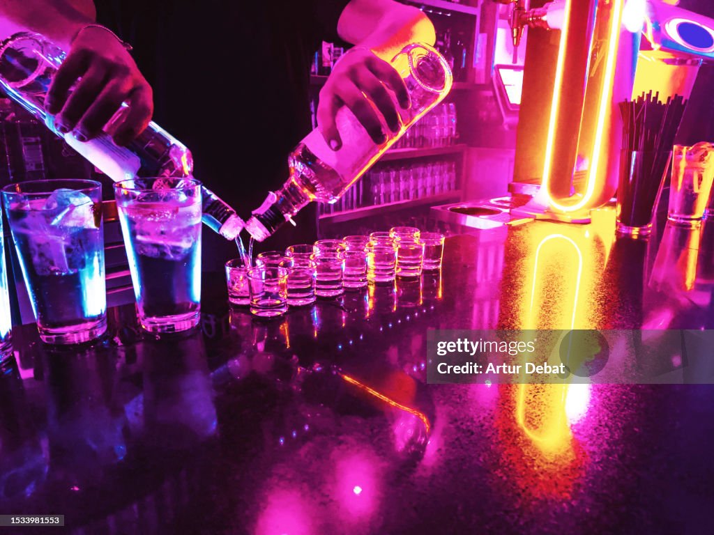 Bartender serving alcohol shots in neon illuminated bar.
