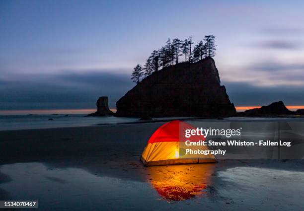 lantern lights up a tent camping with reflections on an ocean beach with clouds and sea stacks in the background - olympic national park stock pictures, royalty-free photos & images