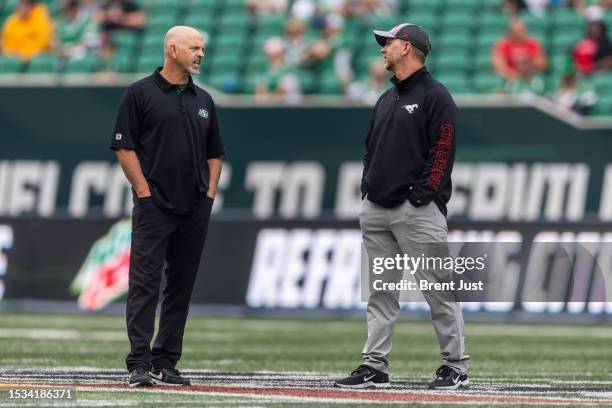 Brothers and head coaches Craig and Dave Dickenson talk on the field before the game between the Calgary Stampeders and Saskatchewan Roughriders at...