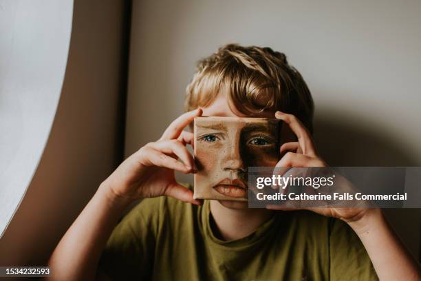 a little boy holds a small oil painting of himself over his face - disguise face stock pictures, royalty-free photos & images