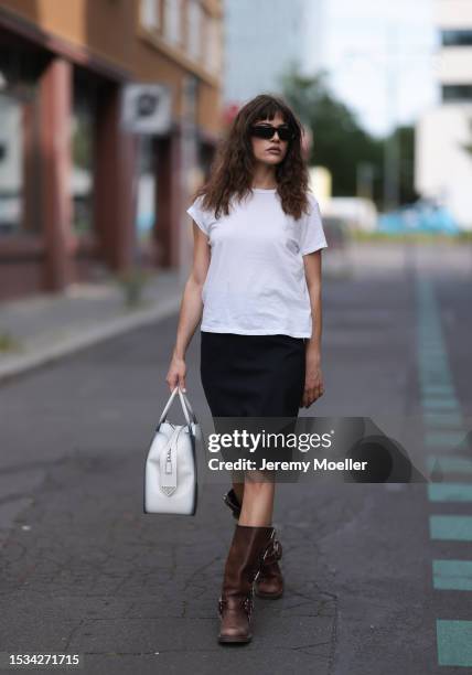 Lea Naumann is seen wearing black sunglasses from Prada, a white tee from Mother Denim, a black knee-length vintage skirt, brown leather boots with...