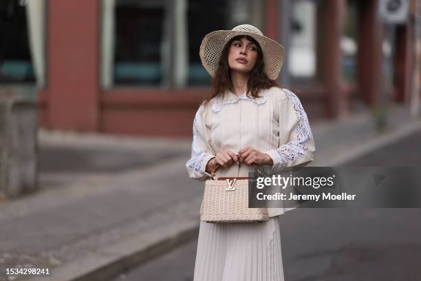 Lea Naumann is seen wearing a natural-colored hat made of palm fibers from Louis Vuitton, a cream-white long-sleeved shirt with white lace details on...