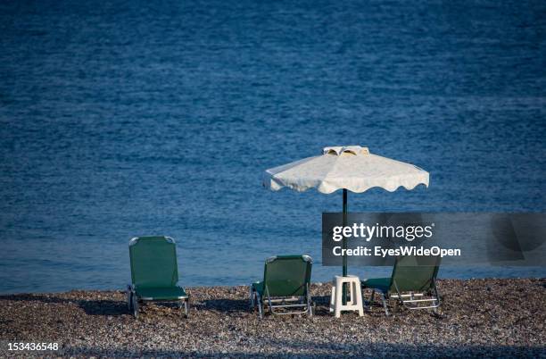 Sunshade, parasol and three lonesome, empty sunchairs, sunbeds at the beach of Kiotari on August 23, 2012 in Rhodes, Greece . Rhodes is the largest...