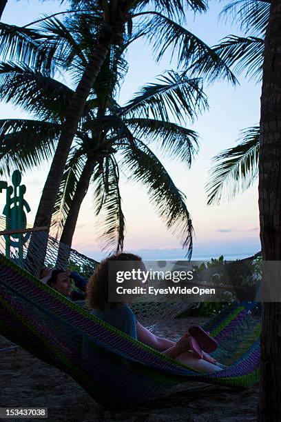 Two women are relaxing in a hammock under palm trees at the beach of Paradise Island while sunset on June 15, 2012 in Nassau, The Bahamas.