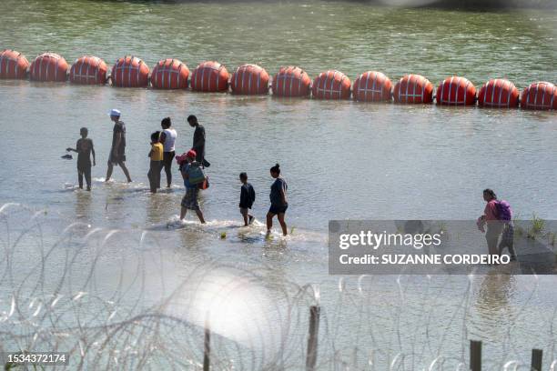 Migrants walk by a string of buoys placed on the water along the Rio Grande border with Mexico in Eagle Pass, Texas, on July 15 to prevent illegal...