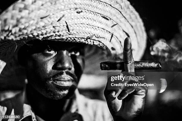 Black and white portrait of a local bahamian man, a smoker, who is wearing a big straw hat and is smoking a cigar at the annual Rake 'n' Scrape...