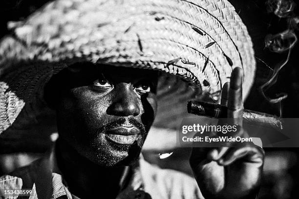 Black and white portrait of a local bahamian man, a smoker, who is wearing a big straw hat and is smoking a cigar at the annual Rake 'n' Scrape...