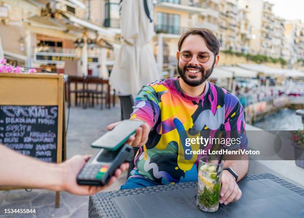man paying with smartphone in a seaside café - malta business stock pictures, royalty-free photos & images