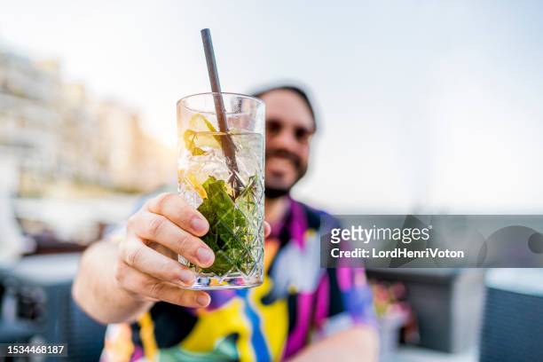 junger mann mit einem cocktail an der bar - tropischer cocktail stock-fotos und bilder