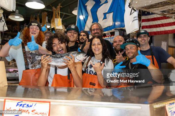 Xolo Maridueña of the film "Blue Beetle" holds a fish while surrounded by Pike Place fishmongers at the Pike Place Market on July 11, 2023 in...