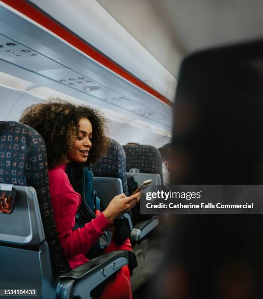 a happy woman uses her mobile phone on a plane - dialogue stock pictures, royalty-free photos & images