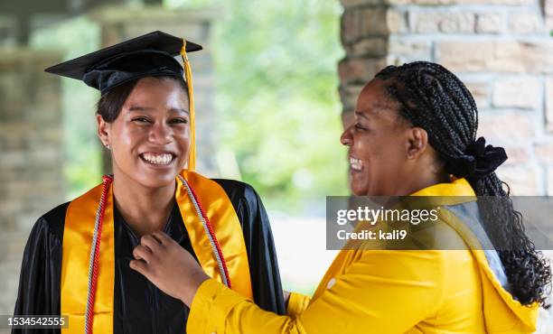 proud mother helping daughter with gown at graduation - laatstejaars high school stockfoto's en -beelden