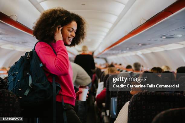 a woman with a backpack boards a small commercial aircraft, greeting a woman who is already seated on the plane - airplane seat stock pictures, royalty-free photos & images
