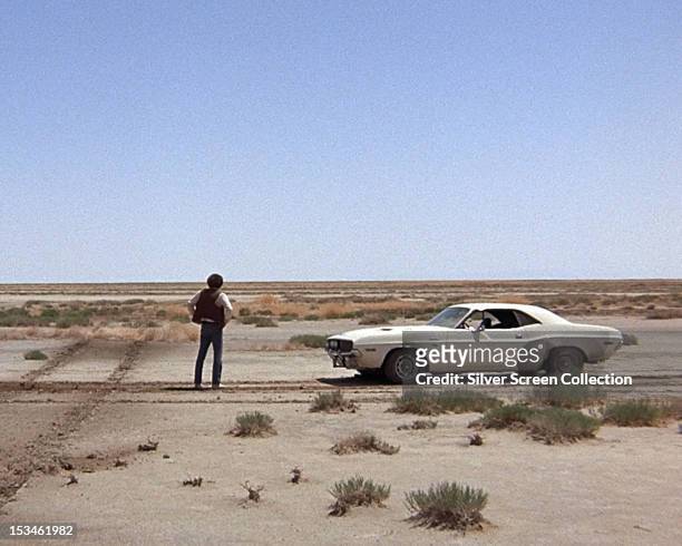 The fugitive Kowalski, played by American actor Barry Newman, stands in the desert next to his Dodge Challenger in a scene from 'Vanishing Point',...