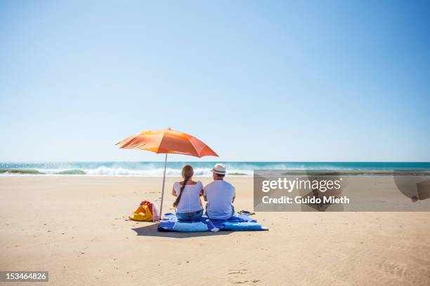 couple looking at sea. - beach umbrella sand stock-fotos und bilder