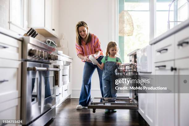 mother and daughter loading dishwasher at home - eletrodoméstico imagens e fotografias de stock