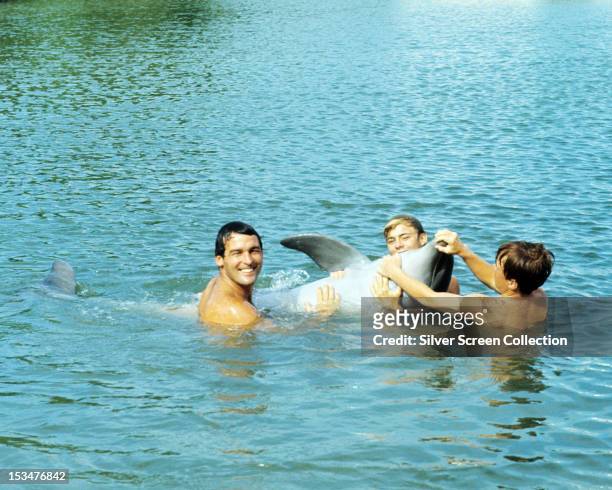 Brian Kelly , Luke Halpin and Tommy Norden as Porter, Sandy and Buck Ricks with a dolphin in the American TV series 'Flipper', circa 1964.