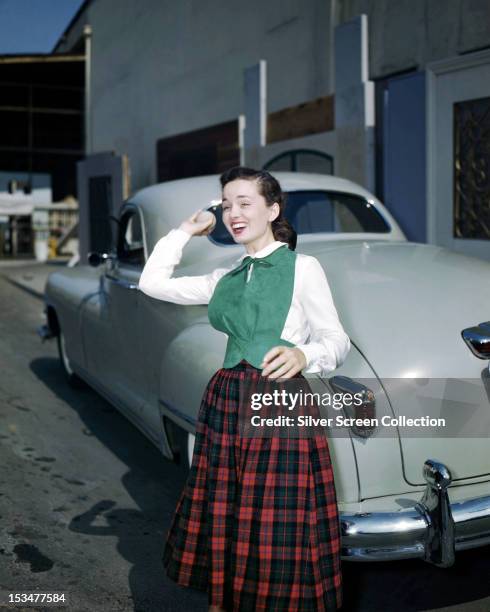American actress and singer Ann Blyth, throwing a ball circa 1945. She is standing next to a car and is wearing a plaid skirt.
