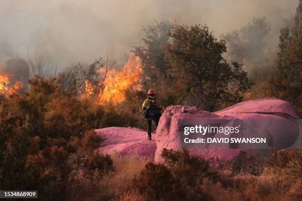 Firefighter stands on boulders covered with pink fire retardant while monitoring the Gavilan Fire, which has already burned more than 250 acres in...