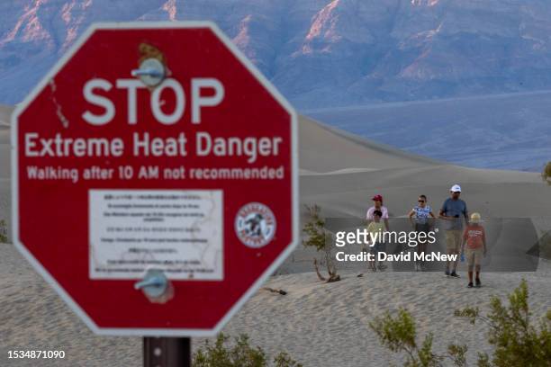 People walk among sand dunes near a sign warning of extreme heat danger on the eve of a day that could set a new world heat record in Death Valley...
