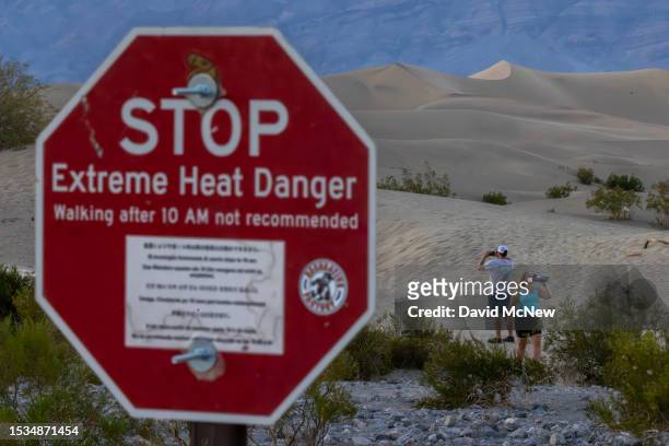 Woman drinks among sand dunes near a sign warning of extreme heat danger on the eve of a day that could set a new world heat record in Death Valley...