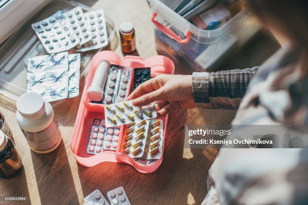 Closeup female hand neatly placing medicament at domestic first aid kit top view. Storage organization in transparent plastic box drug, pill, syringe, bandage. Fast health help safety emergency supply
