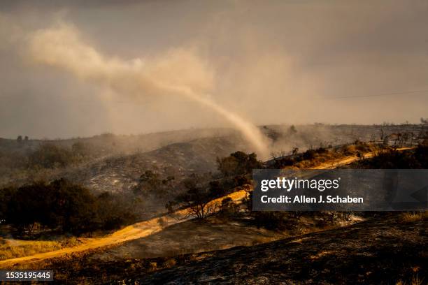 Riverside County, CA After a water-dropping helicopter flew overhead to make a drop nearby, a smoke funnel spins across the scorched landscape after...