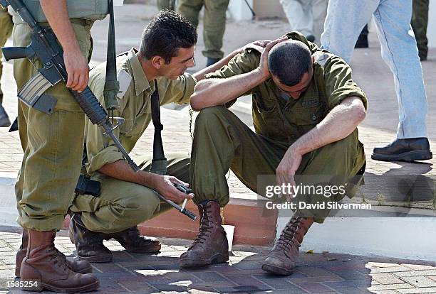 Israeli soldiers comfort a grieving comrade at the scene of a Palestinian suicide bombing October 27, 2002 at the entrance to the West Bank Jewish...