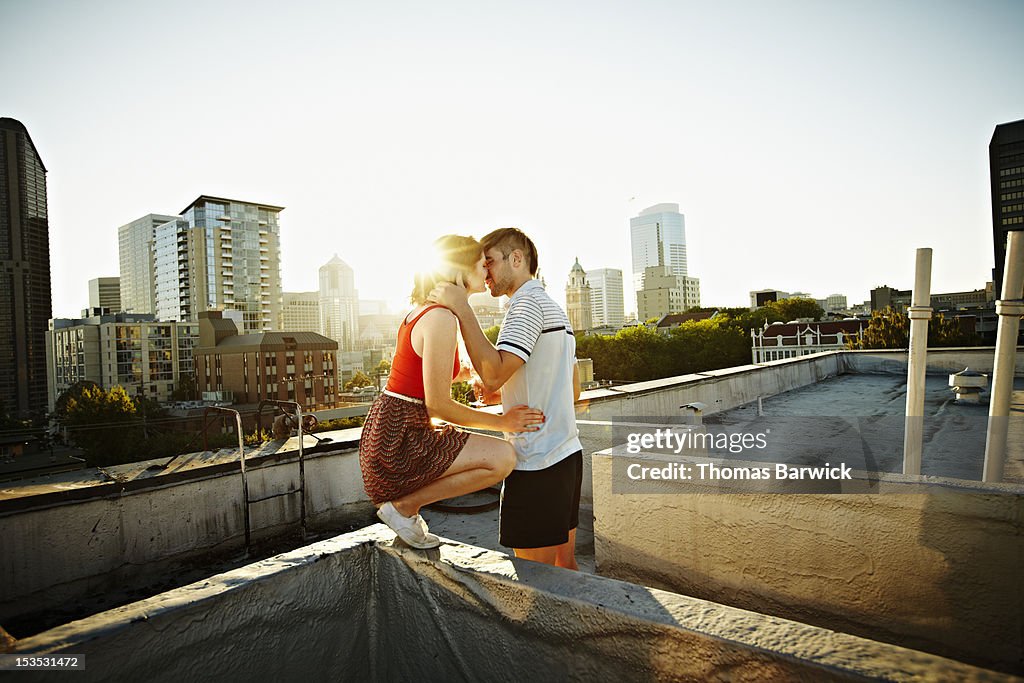 Couple kissing on rooftop of building at sunset