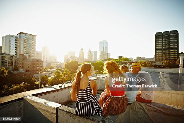 group of friends sitting on roof at sunset - sunset freinds city stock-fotos und bilder