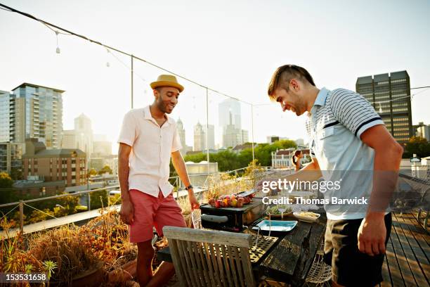 two friends standing at barbecue on rooftop deck - rooftop bbq stock pictures, royalty-free photos & images