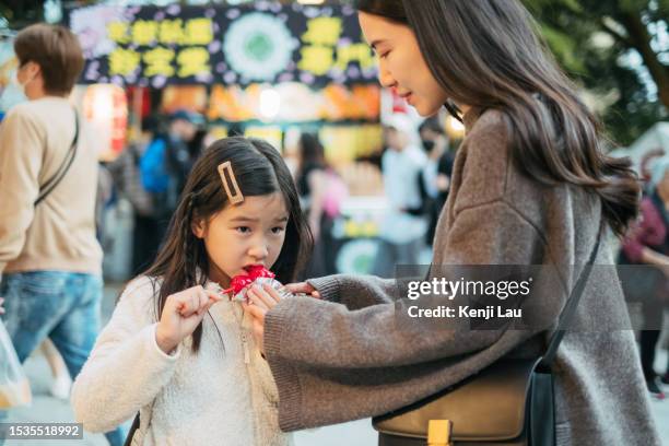 young asian mother taking care her little daughter and assisting her to eat traditional japanese street food while travelling to japan. concept of street food, eating, carefree, childhood, vacation, family day, local foodie experience. - child foodie photos et images de collection