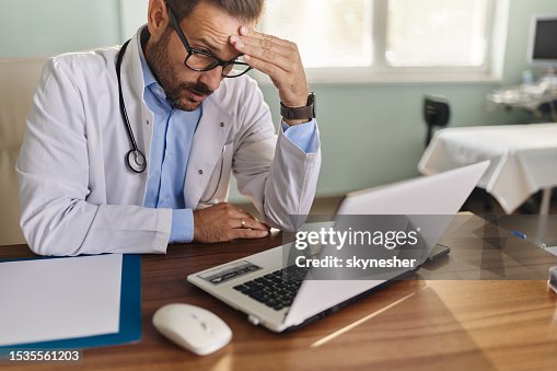 Médico preocupado leyendo un correo electrónico en una computadora portátil en la oficina. Médico preocupado leyendo un correo electrónico en una computadora portátil en la oficina.