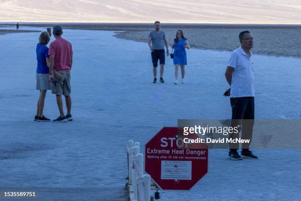 People walk on salt flats before the arrival of the early morning sun near a sign warning of extreme heat danger at Badwater, the lowest point in...