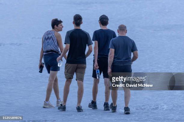 People walk on salt flats before the arrival of the early morning sun near a sign warning of extreme heat danger at Badwater, the lowest point in...