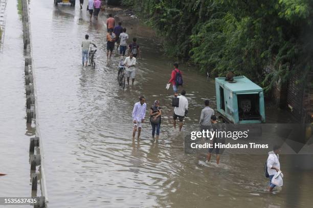 People are going to their workplace cross a waterlogged stretch after the rain at National Highway-48 near Narsinghpur village, on July 16, 2023 in...