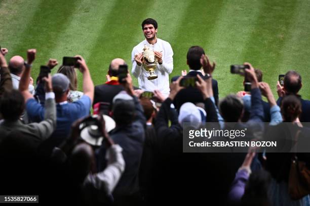 Spain's Carlos Alcaraz holds the winner's trophy as he smiles to the stands after beating Serbia's Novak Djokovic during their men's singles final...