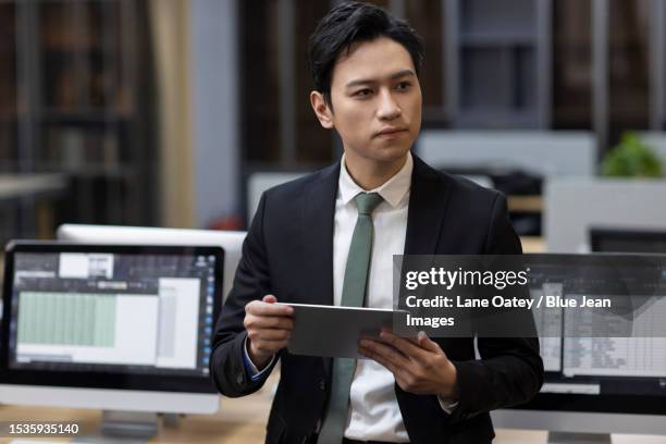 young chinese businessman holding a digital tablet in office - businesswear stock pictures, royalty-free photos & images