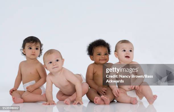 four multiethnic babies sitting on white. - sólo bebés fotografías e imágenes de stock