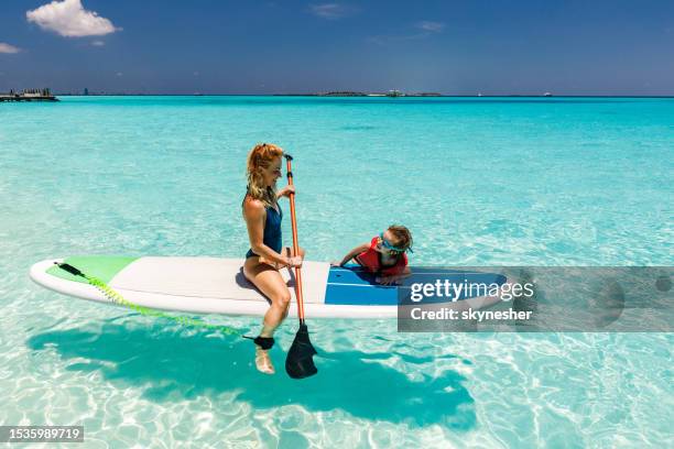 happy single mother and her son talking on a paddleboard in sea. - maldives sport stock pictures, royalty-free photos & images